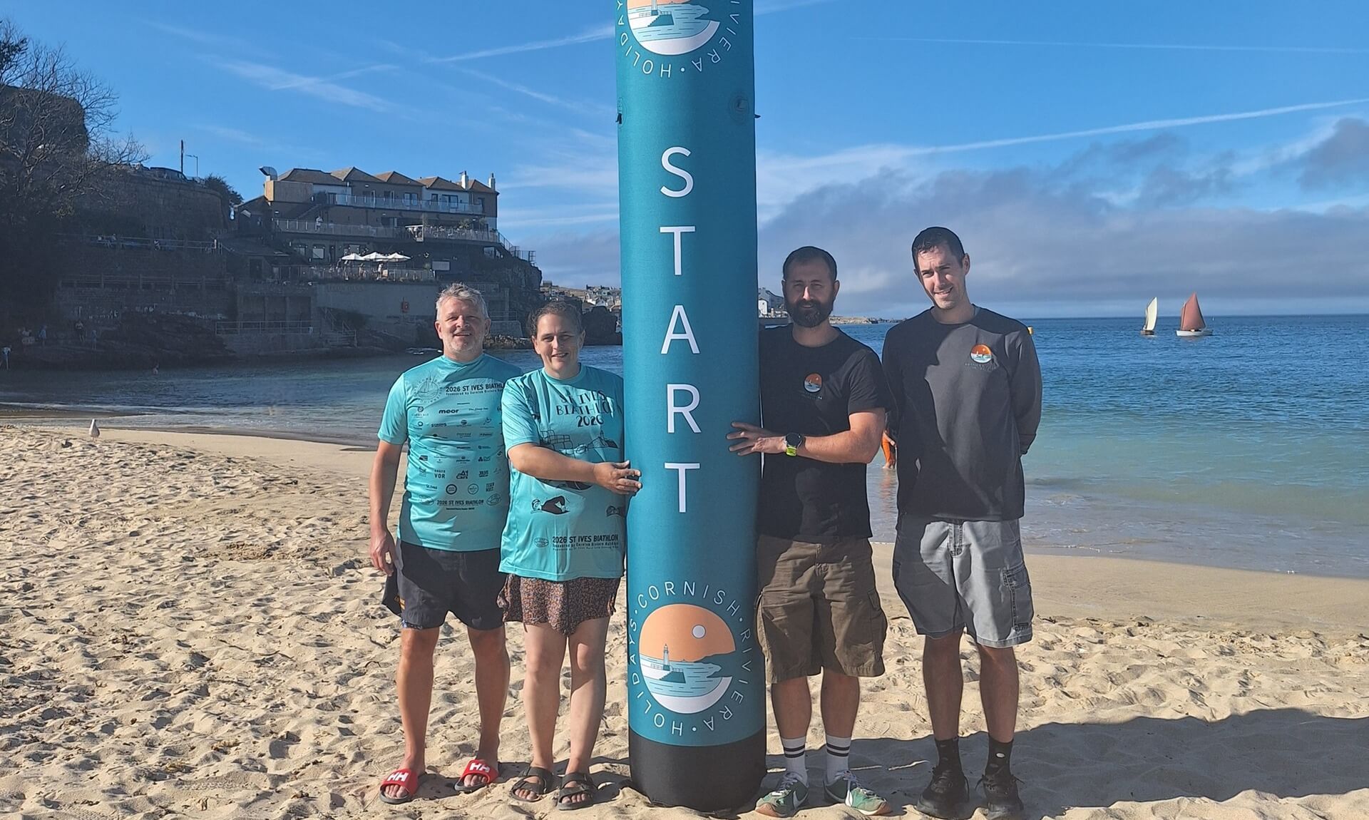 Four St Ives Surf Life Saving Club members beside the inflatable Biathlon start marker on the beach at St Ives