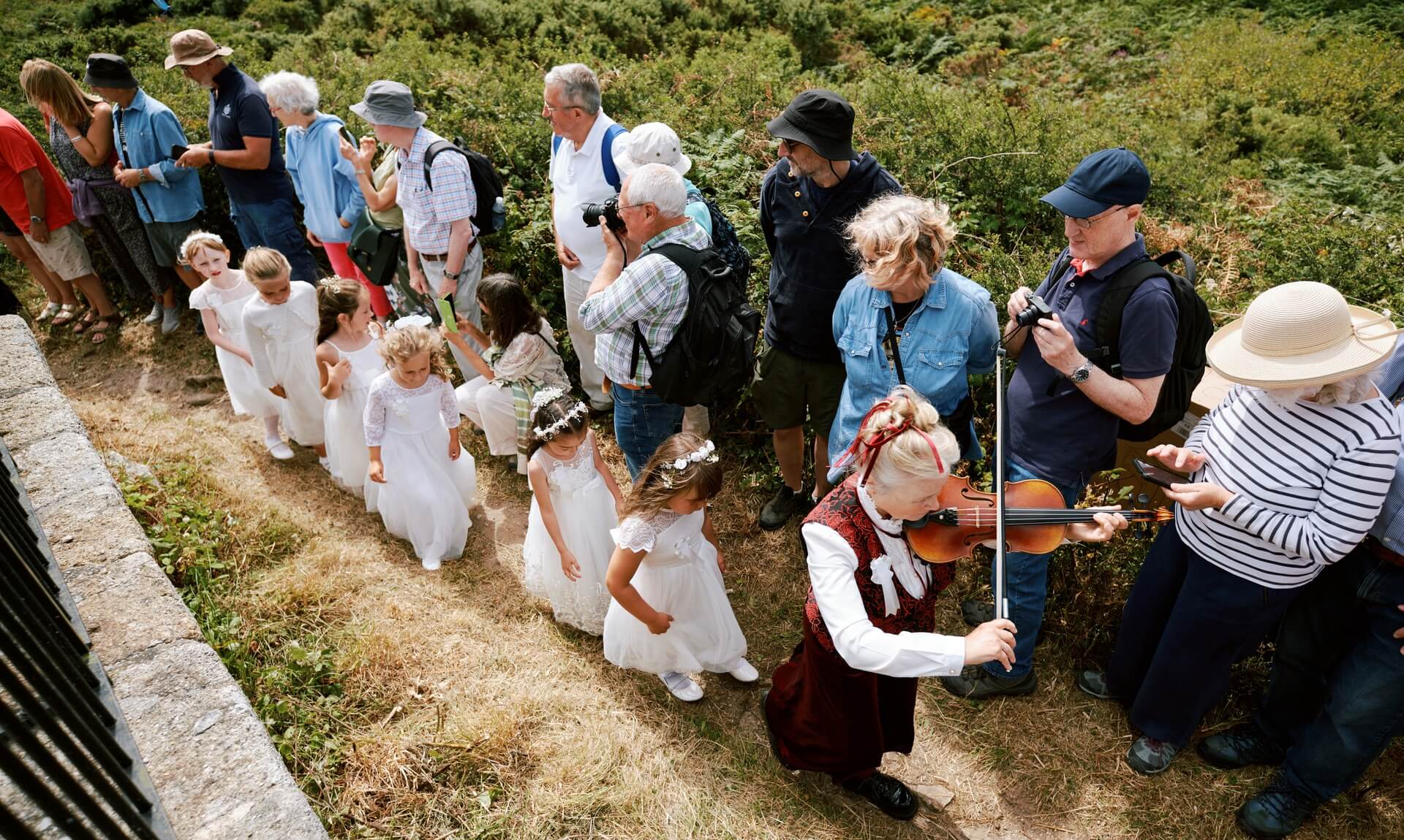 A fiddler in red velvet leads maids in white past a crowd on Worvas Hill above St Ives