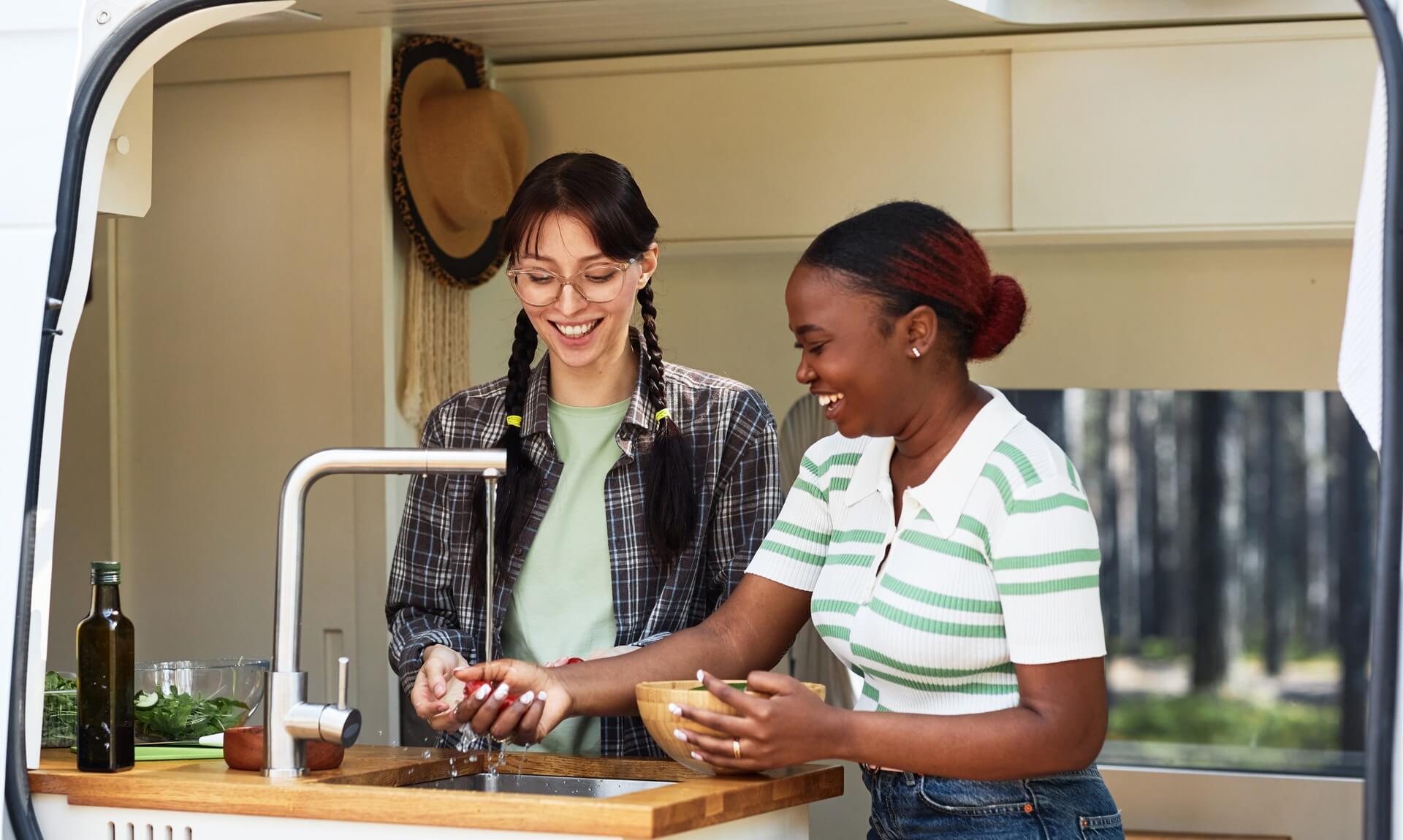Two women washing vegetables at an outdoor campervan sink