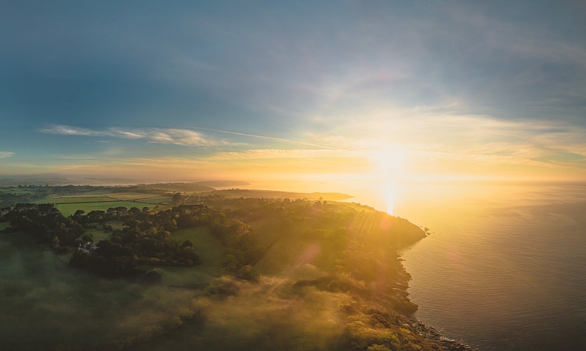 Aerial view of the Helford coast at sunrise, with a wooded headland, fields and the sea near Helford Passage