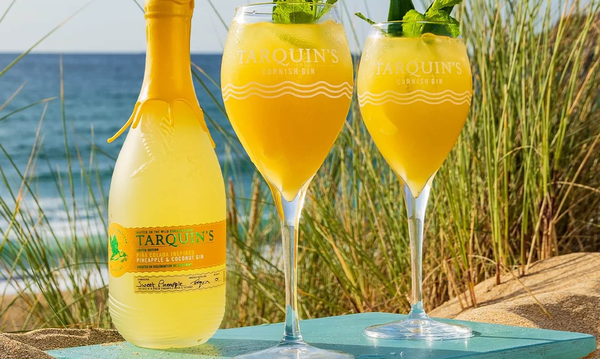 Tarquin's Piña Colada gin bottle and two cocktails on a beach