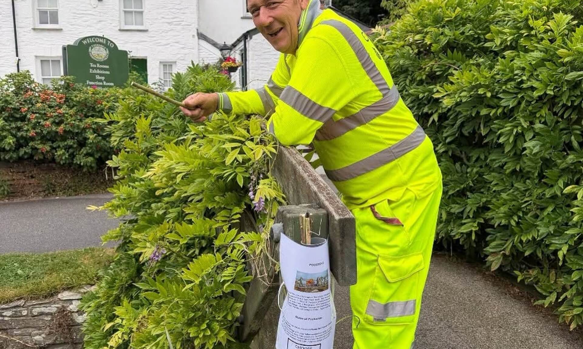 A gardener in hi-vis leaning over the Wisteria Bridge at Trenance Gardens, with a stick holder fixed to the bridge post