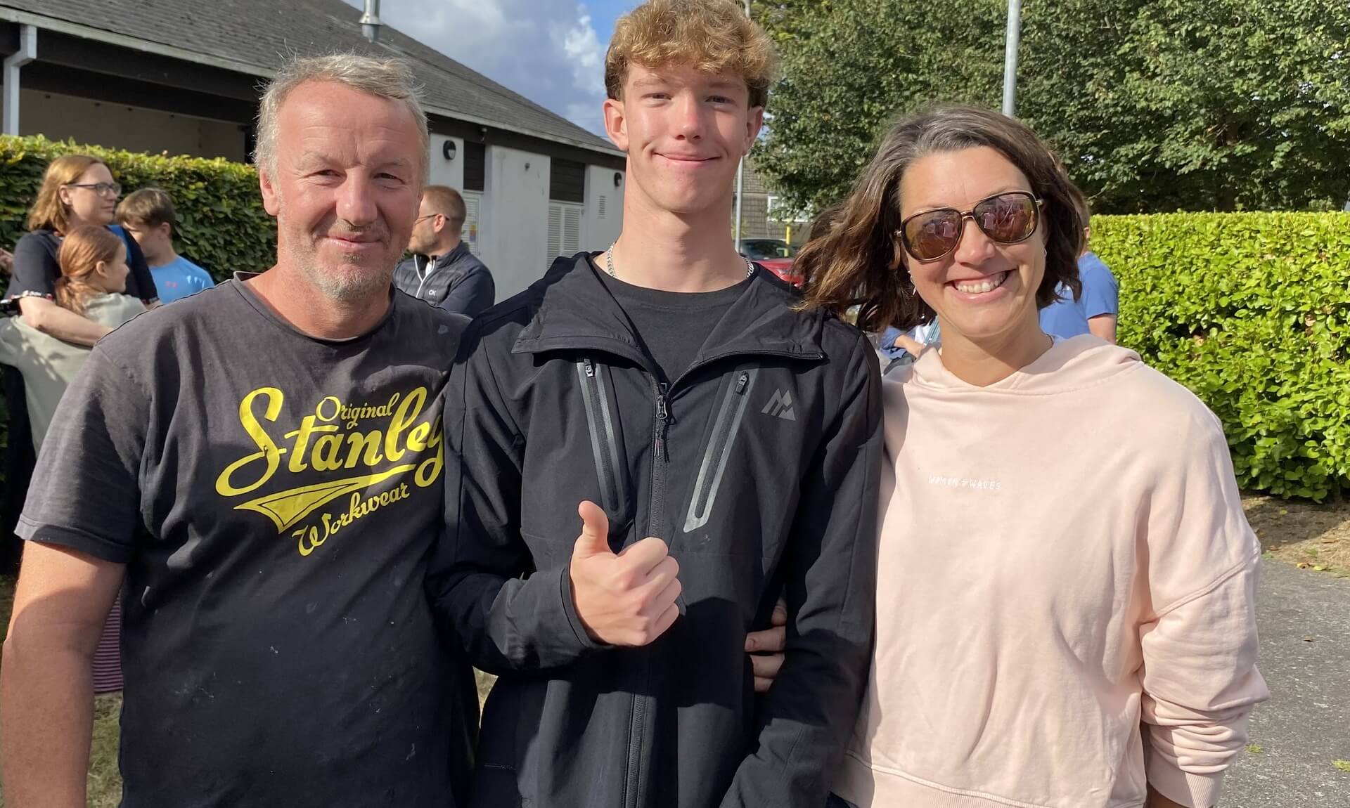 A Treviglas Academy student giving a thumbs up between two family members on GCSE results day