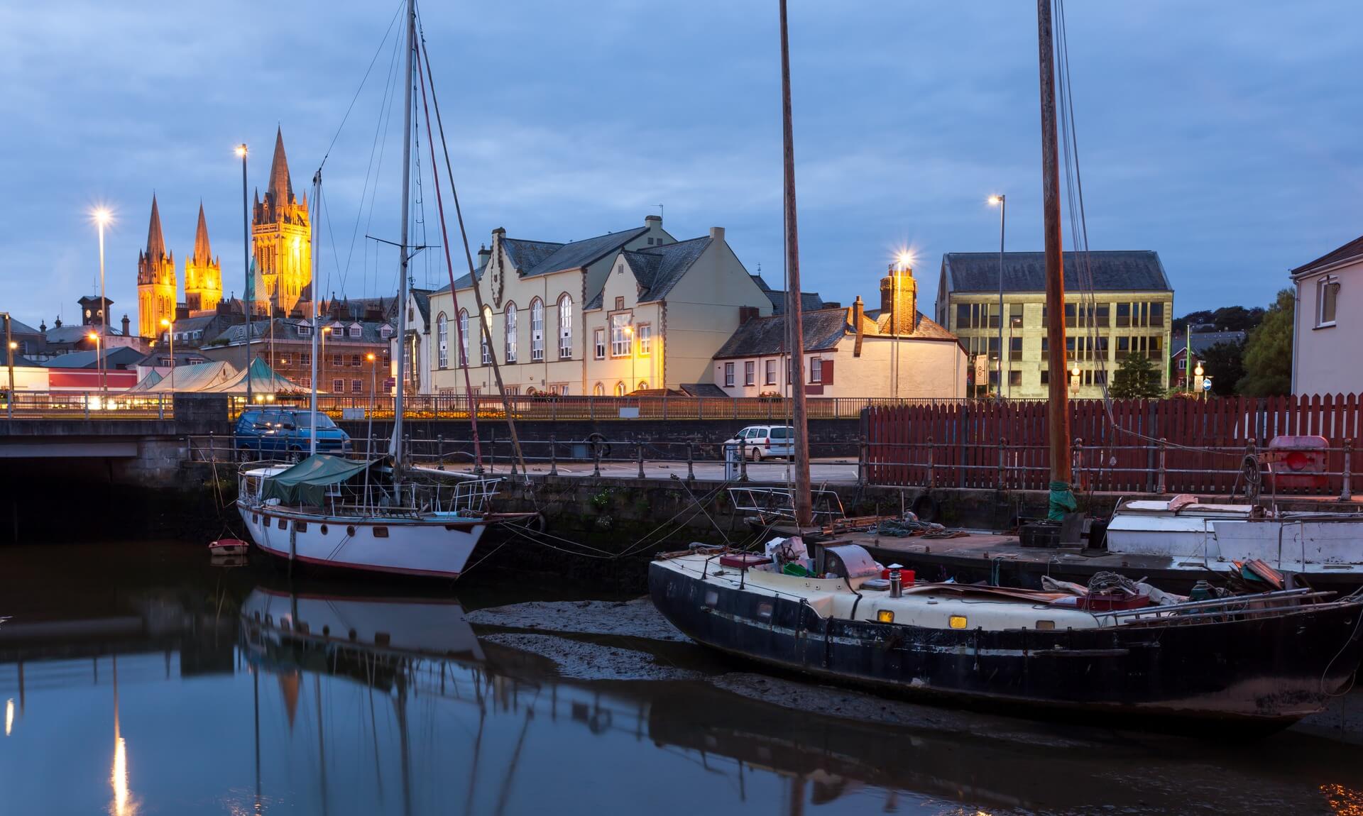 Truro harbour at dusk with boats moored on the tide and the cathedral lit behind