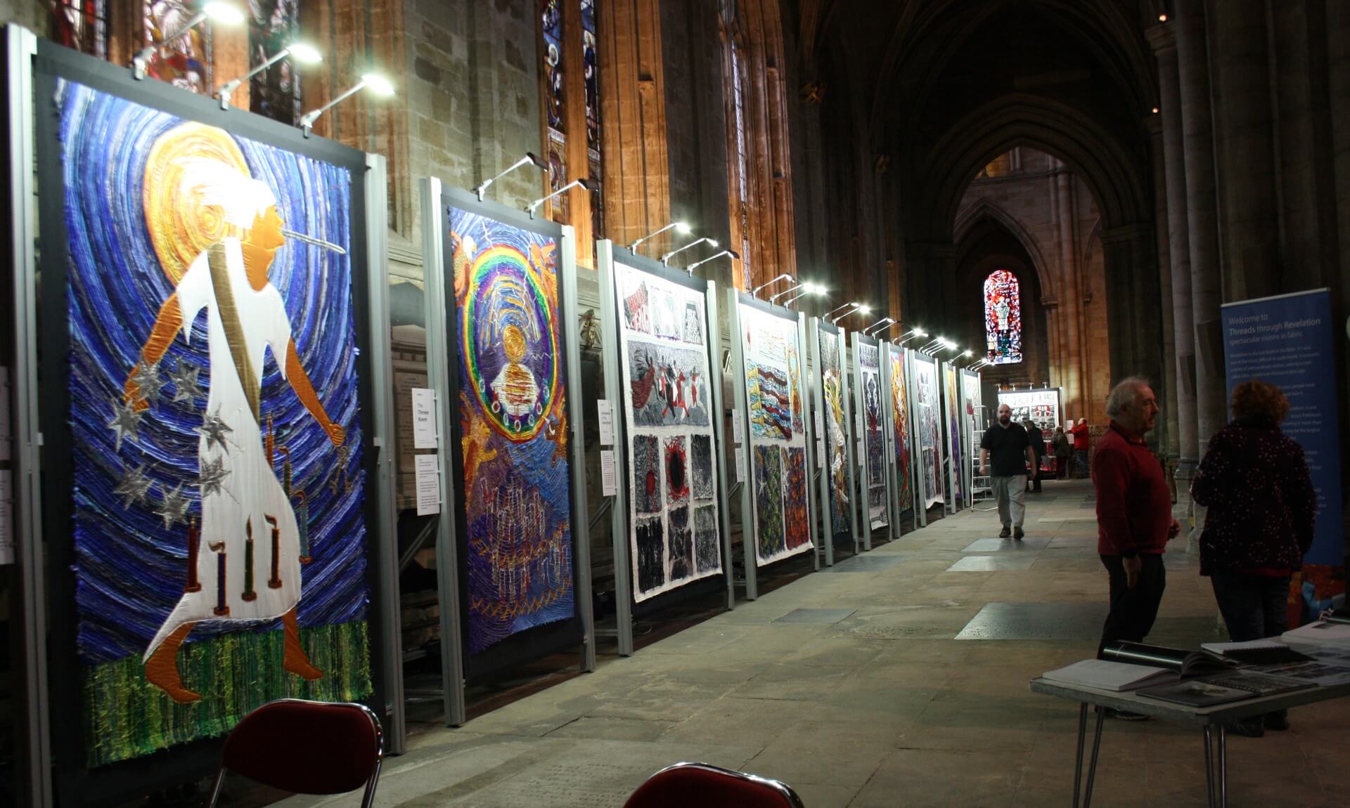 Row of huge embroidered silk panels lit along Truro Cathedral's nave