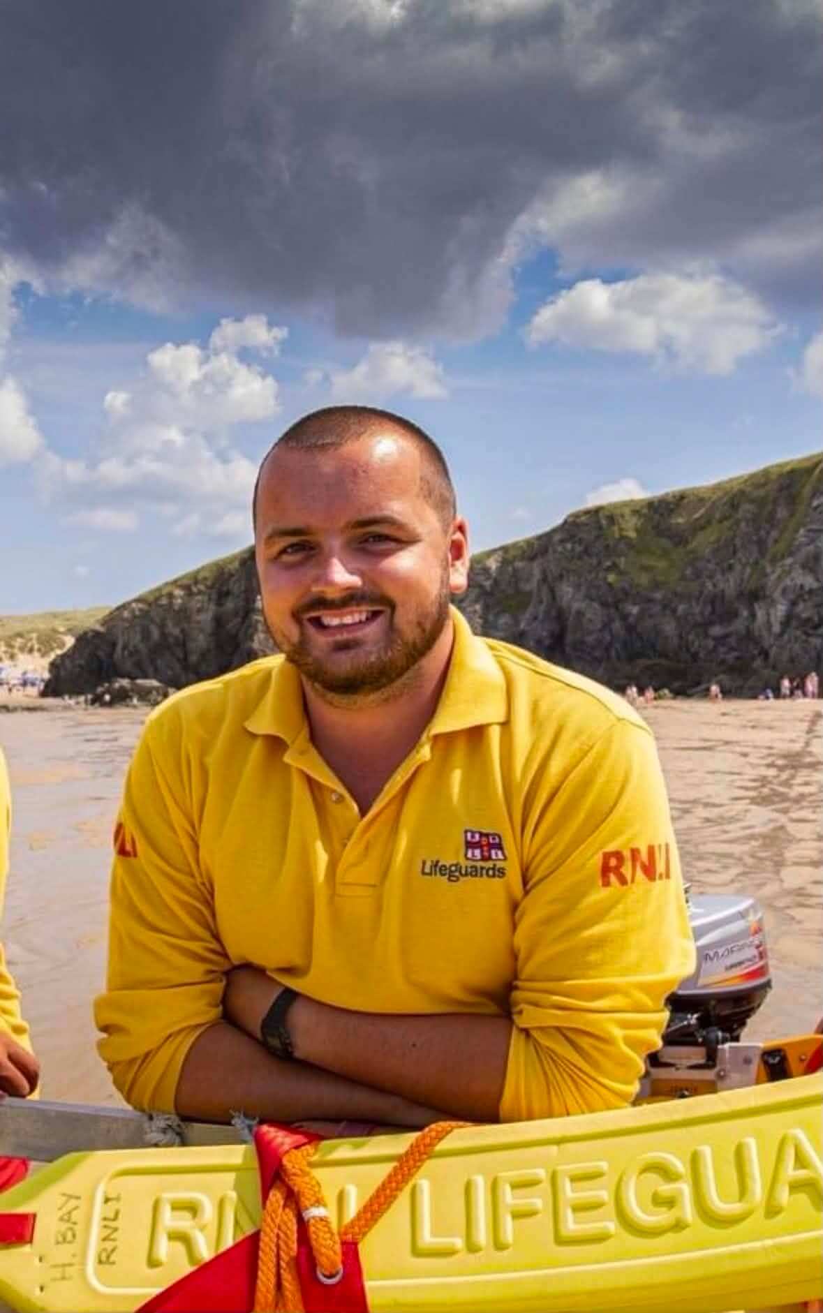 Matt Trewhella in RNLI Lifeguards uniform on the beach beside a rescue craft