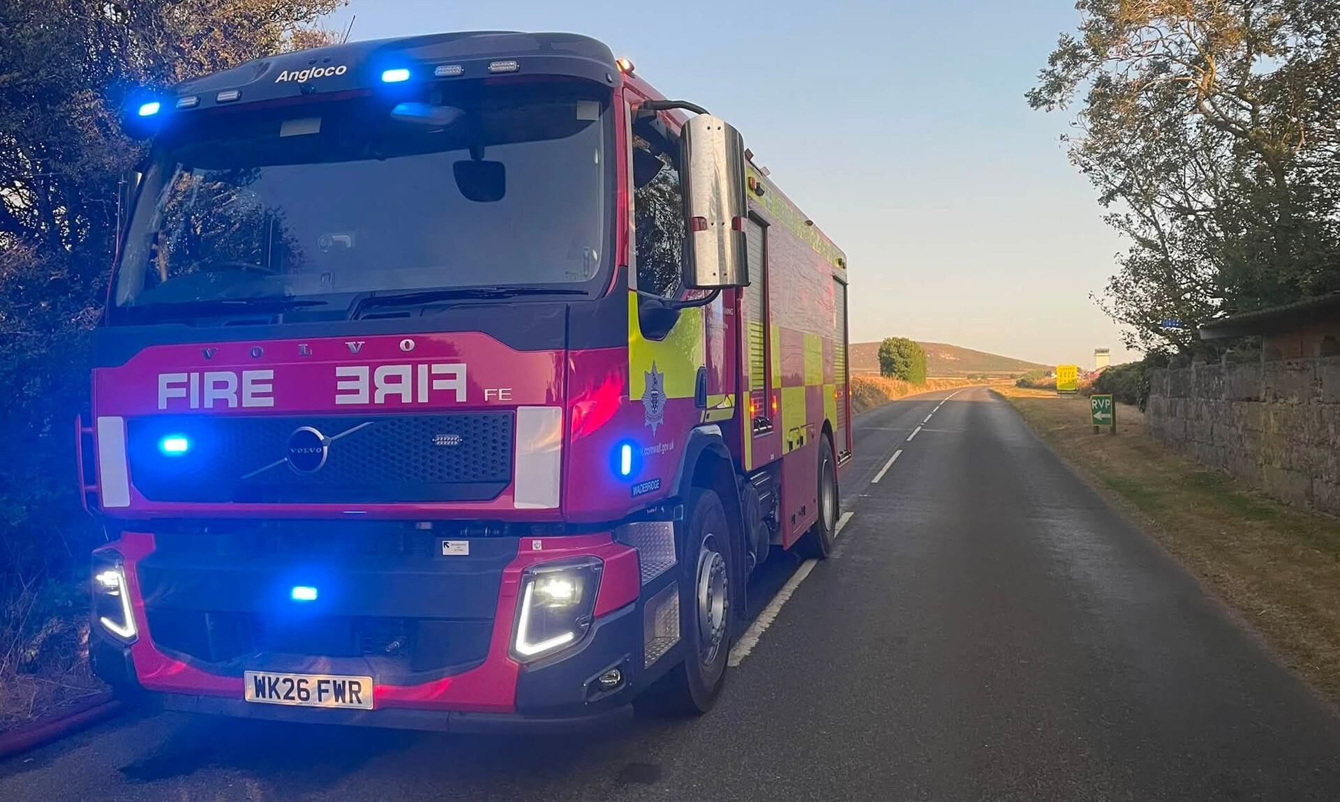 A Cornwall Fire and Rescue Service engine parked on a rural road near Wadebridge at dusk with its blue lights on