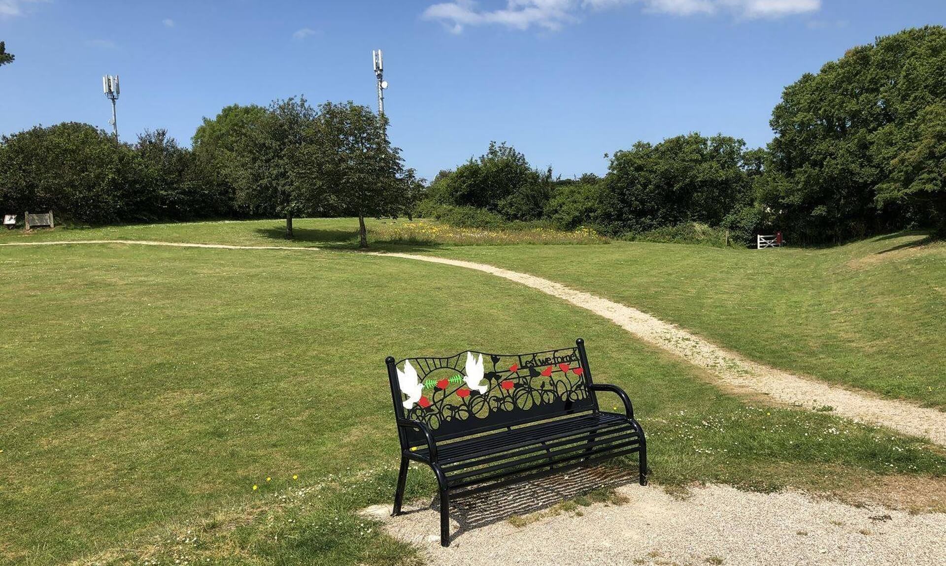 A park in Wadebridge with wildflowers, a gravel path and a memorial bench