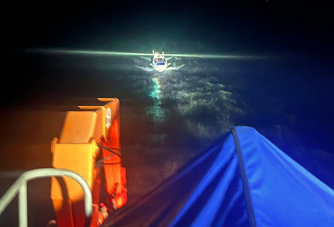 Penlee RNLI all-weather lifeboat approaches the rowing boat at night, lit by searchlight
