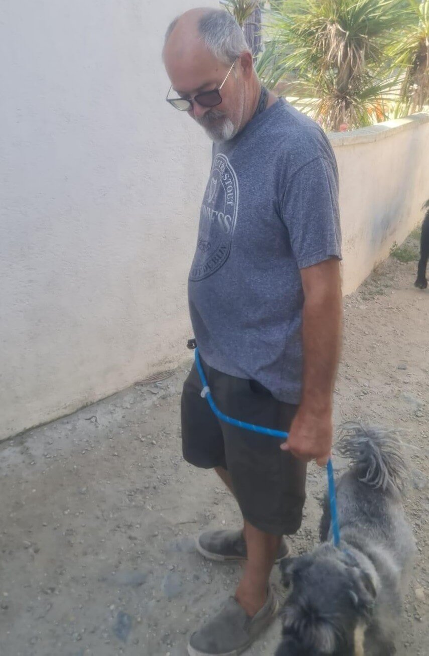 A man walking a small grey dog on a blue lead