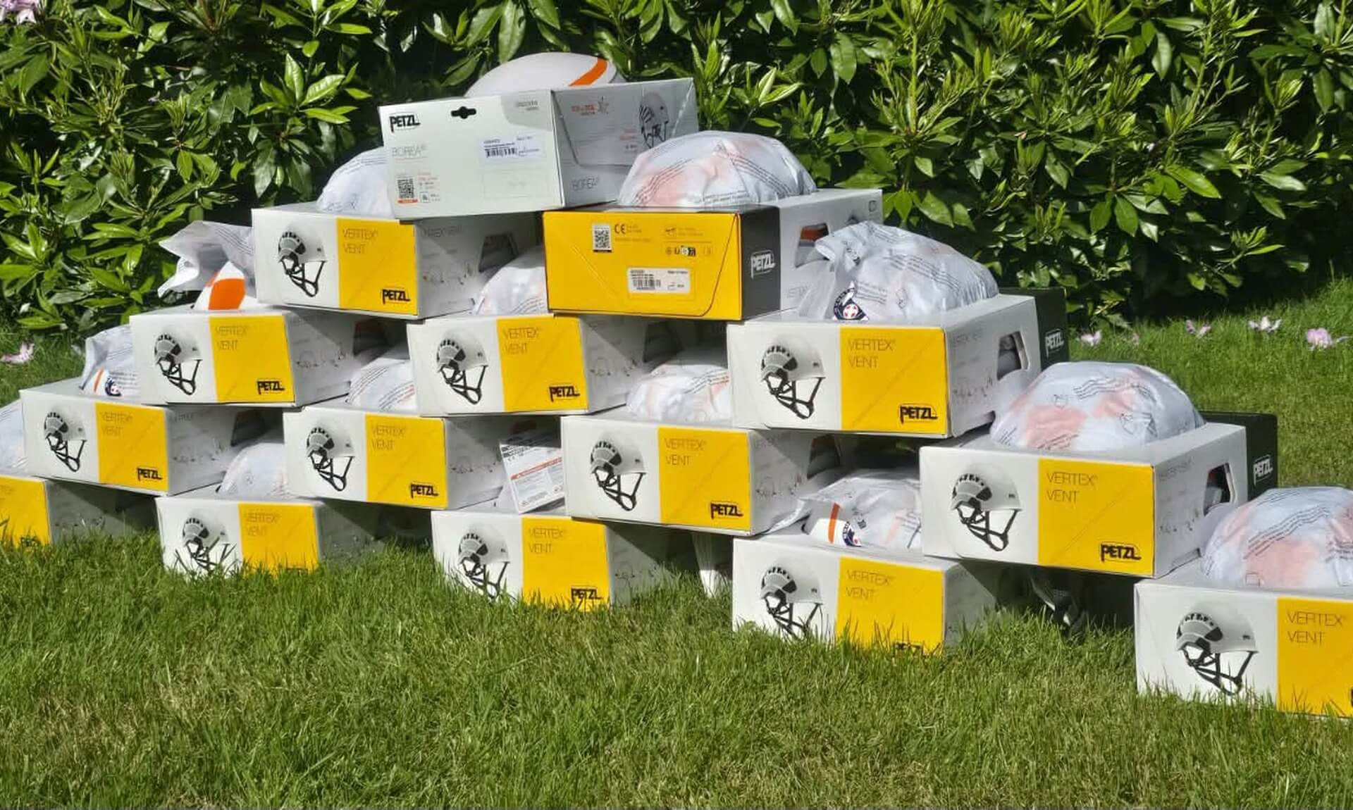 A pyramid of boxed Petzl Vertex Vent helmets stacked on a lawn