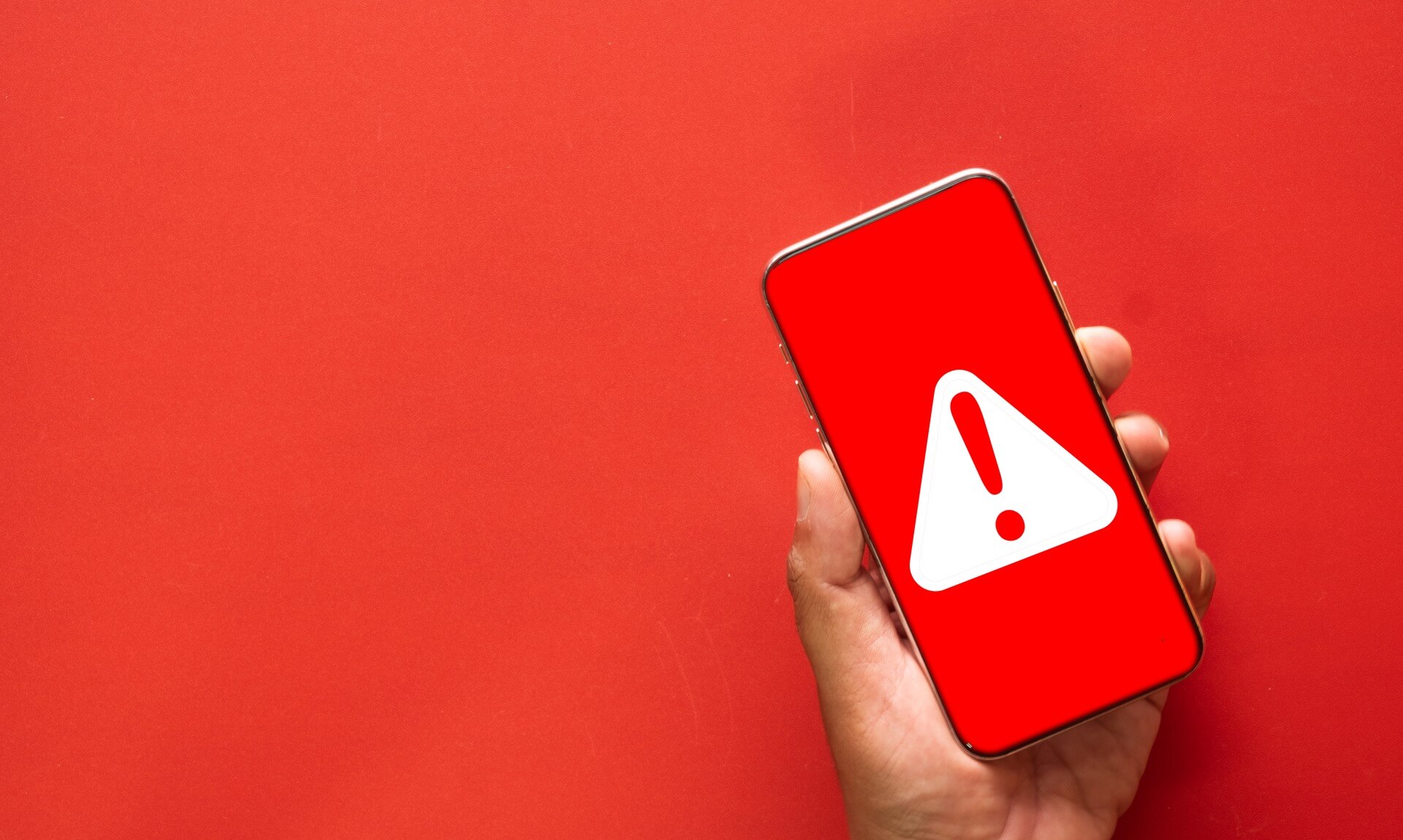 A hand holding a smartphone showing a red emergency alert screen with a white warning triangle