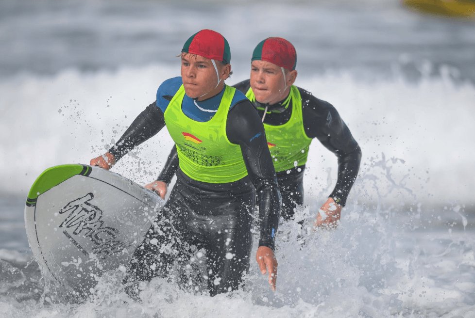 Two young competitors running through the surf with a bodyboard