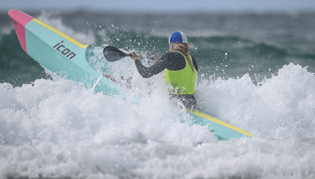 A competitor battling through a wave on a surf ski