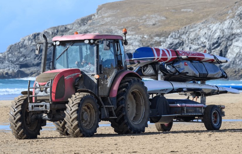 A tractor towing beach lifesaving equipment across Holywell Bay
