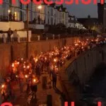 Crowds carrying lit torches along Porthleven harbour wall at night