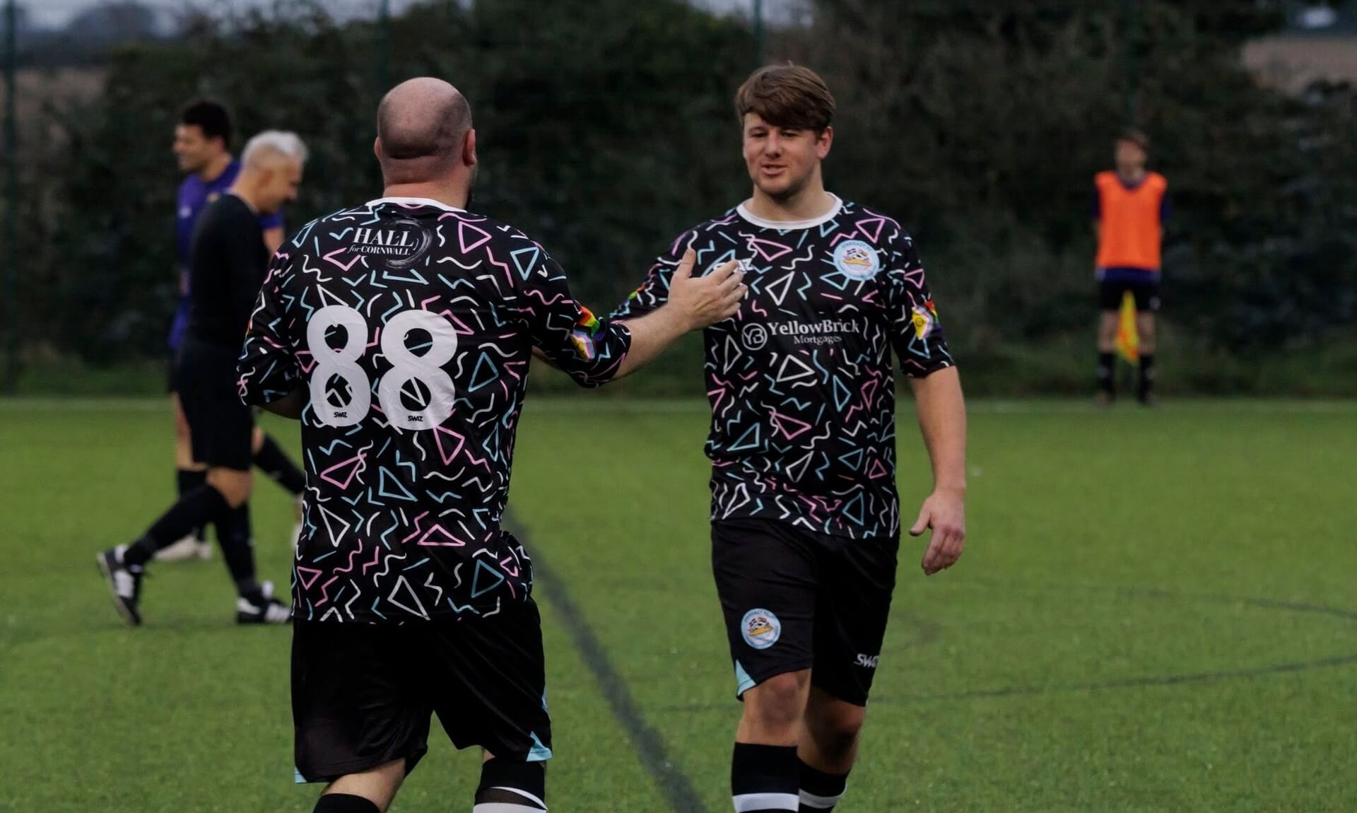 Two Stargazy FC players in the club's 80s-pattern kit with Pride armbands, one wearing number 88, on the pitch