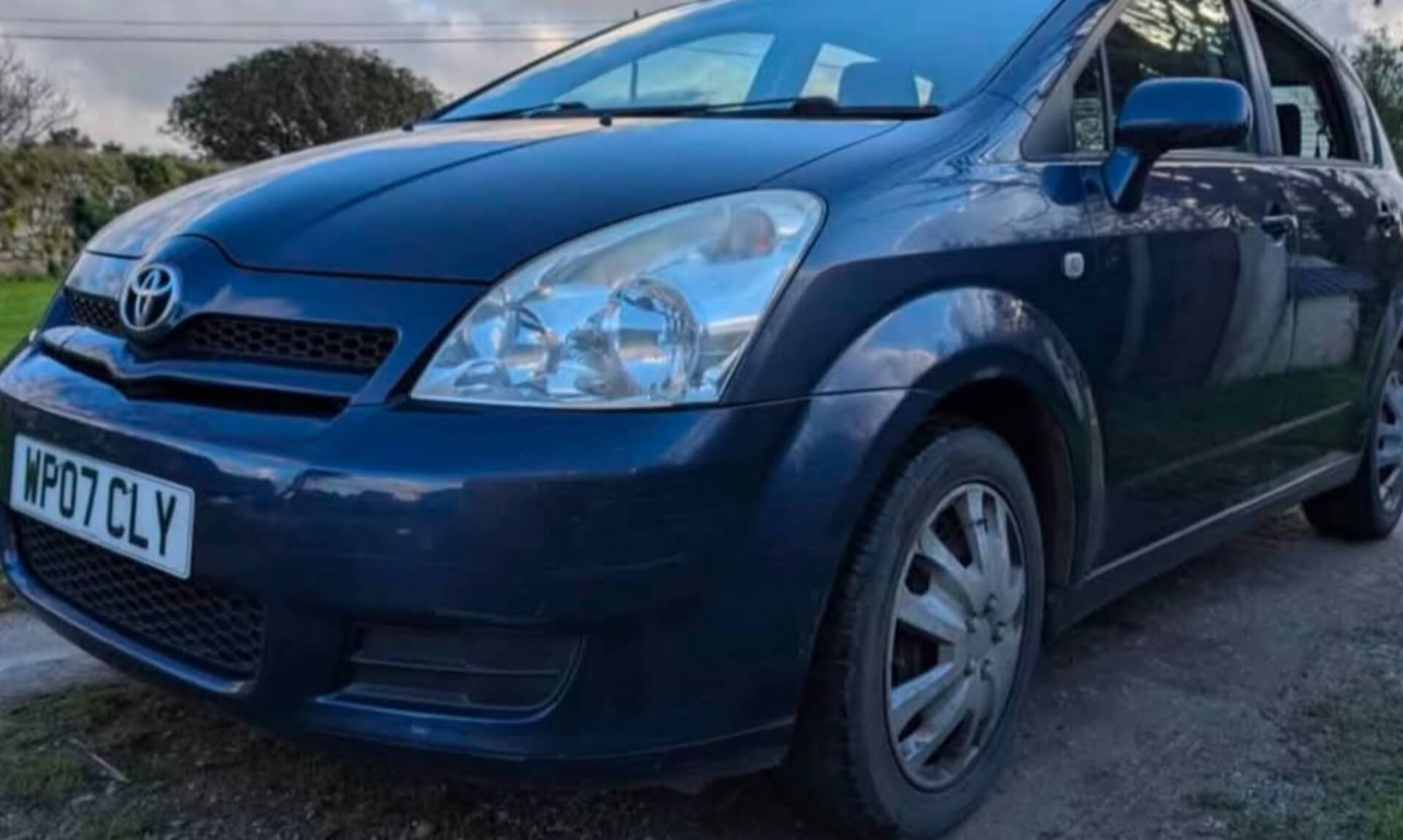 An ageing dark blue Toyota parked on a rural Cornwall driveway, the questionable car being driven to Benidorm for charity