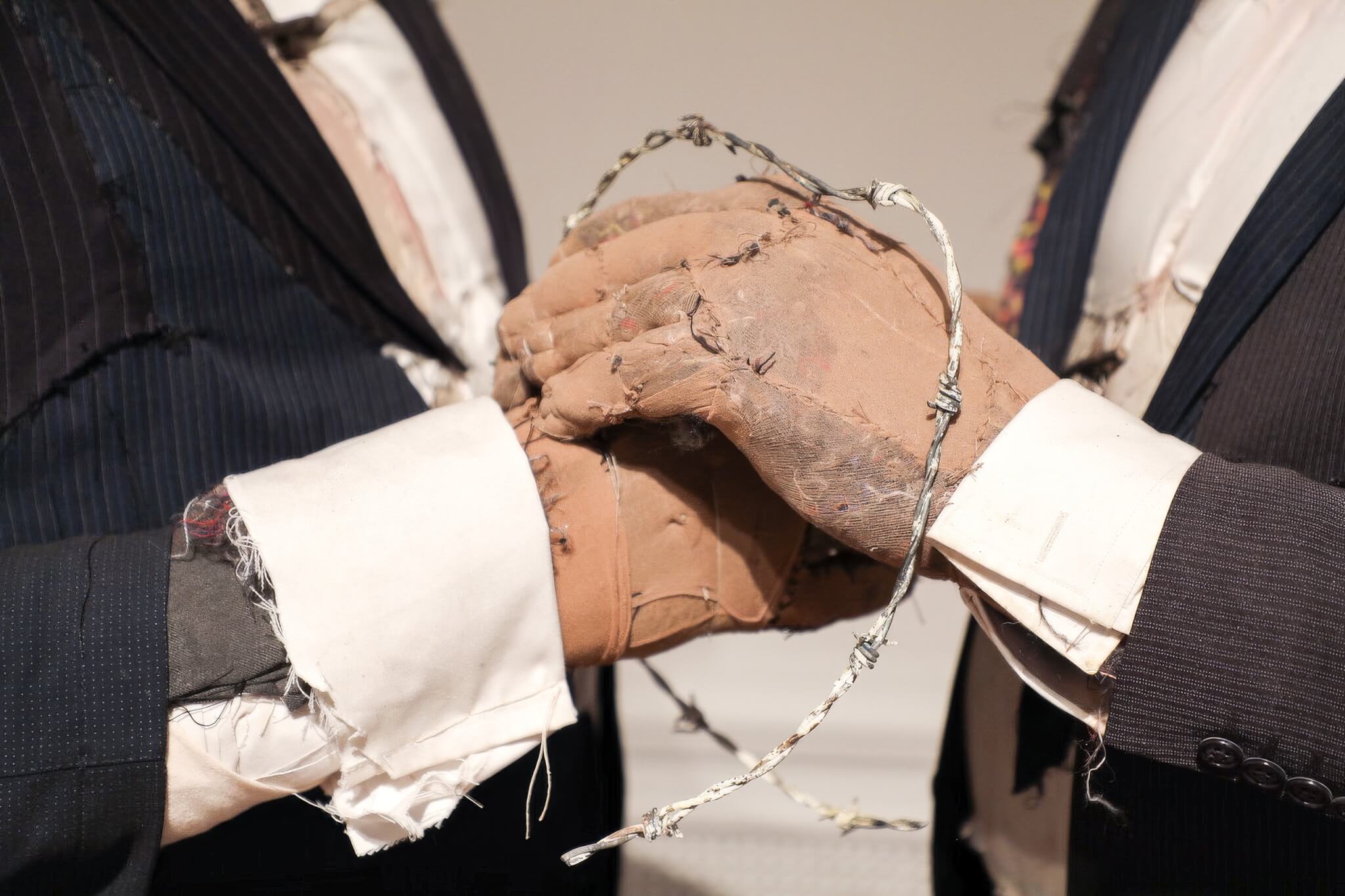 Sewn fabric hands clasped inside a loop of barbed wire in Tim Shaw's sculpture Pin It On Them