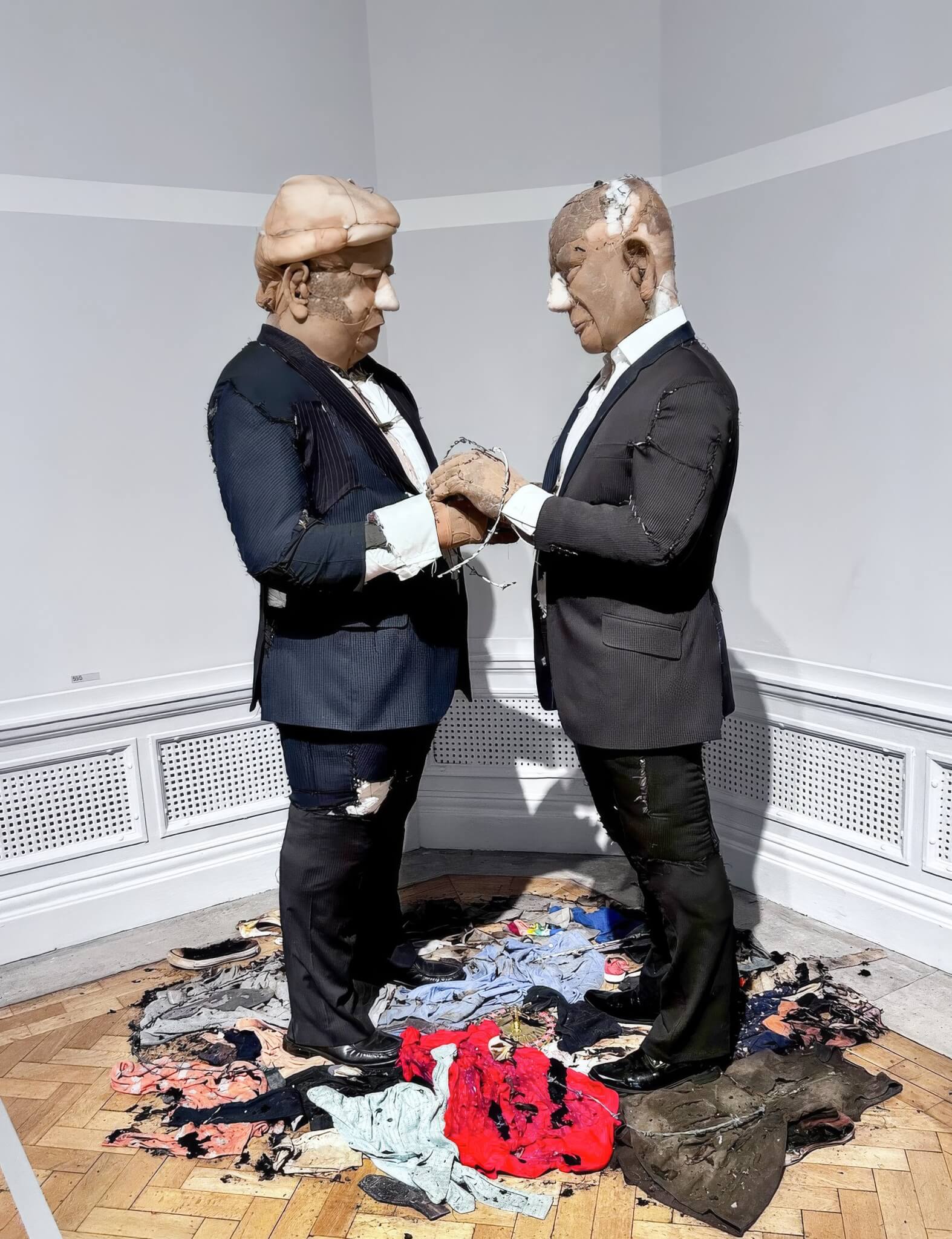 Full view of Pin It On Them, two suited figures holding hands above burnt clothing
