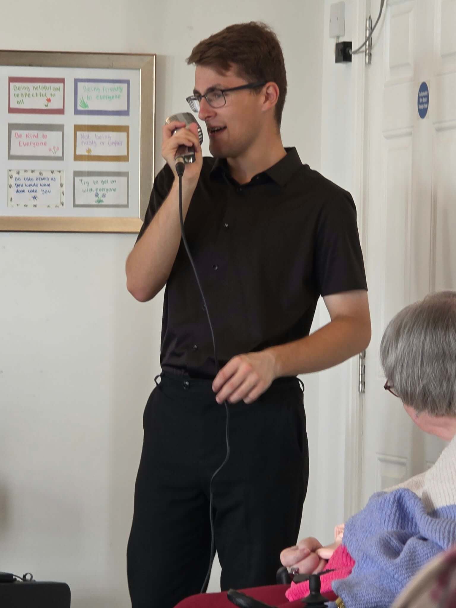 Jacob Reed singing into a vintage microphone at a care home, with a resident watching