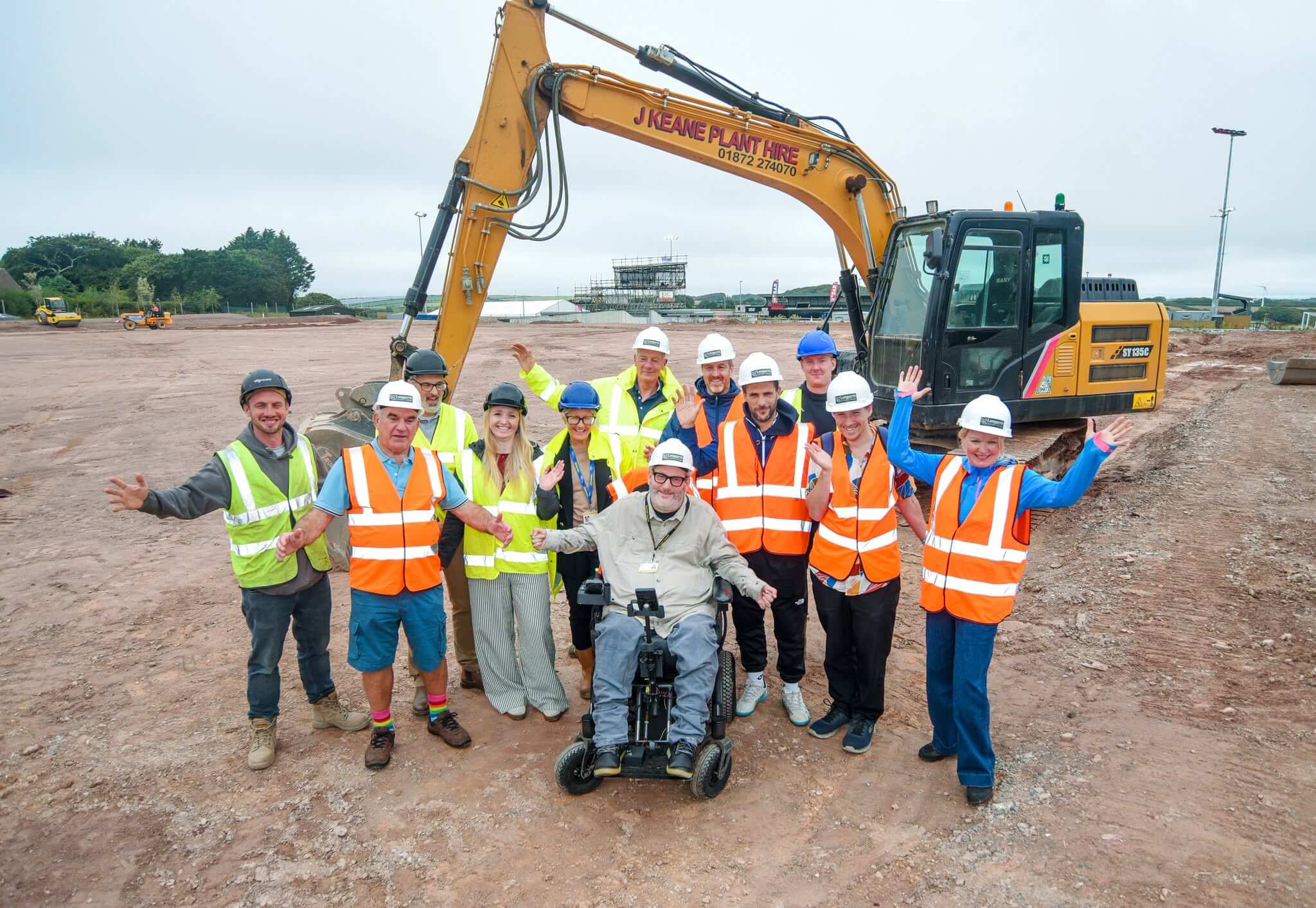 Group in hard hats and hi-vis in front of a digger at the Truro Sports Hub 3G pitch site, Langarth