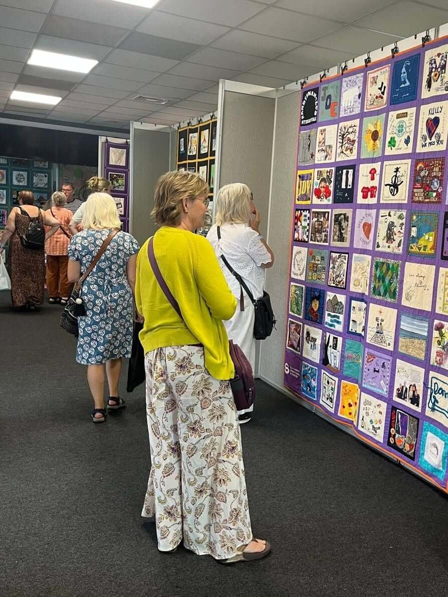 Visitors browsing a row of Speak Their Name memorial quilts