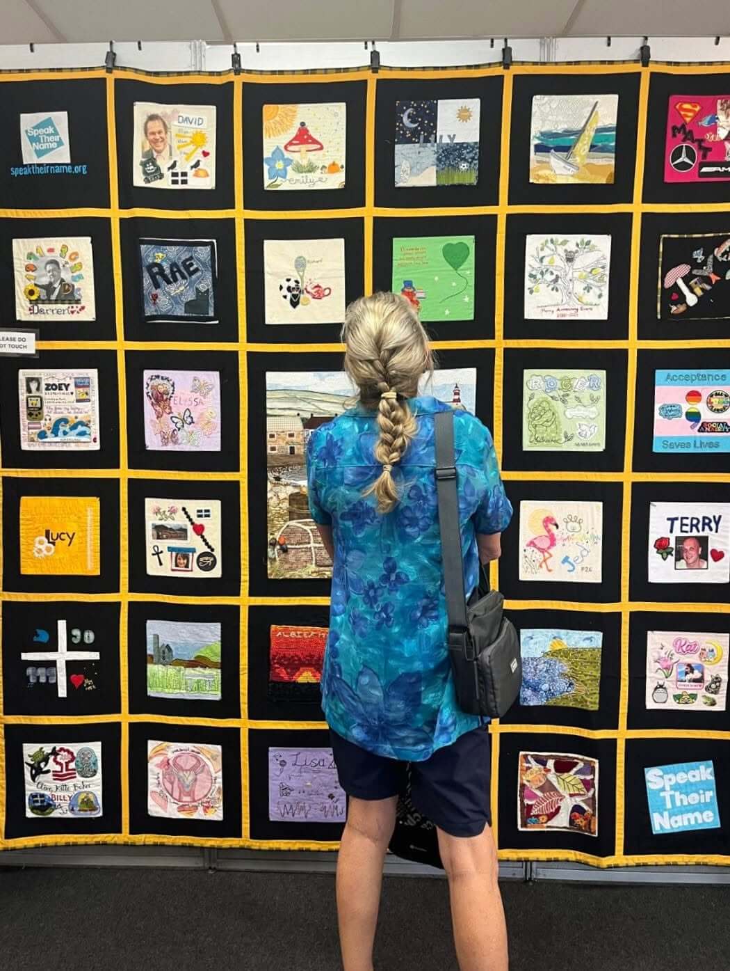 Visitor looking at a wall of Speak Their Name memorial quilt squares