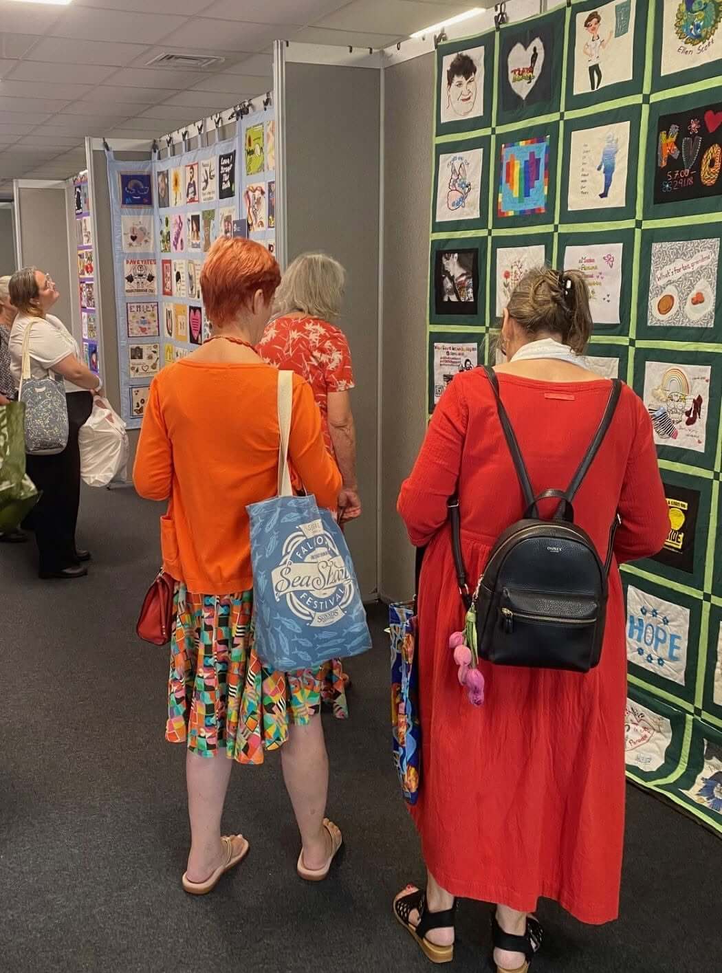 Two visitors looking at a green-bordered Speak Their Name memorial quilt reading HOPE