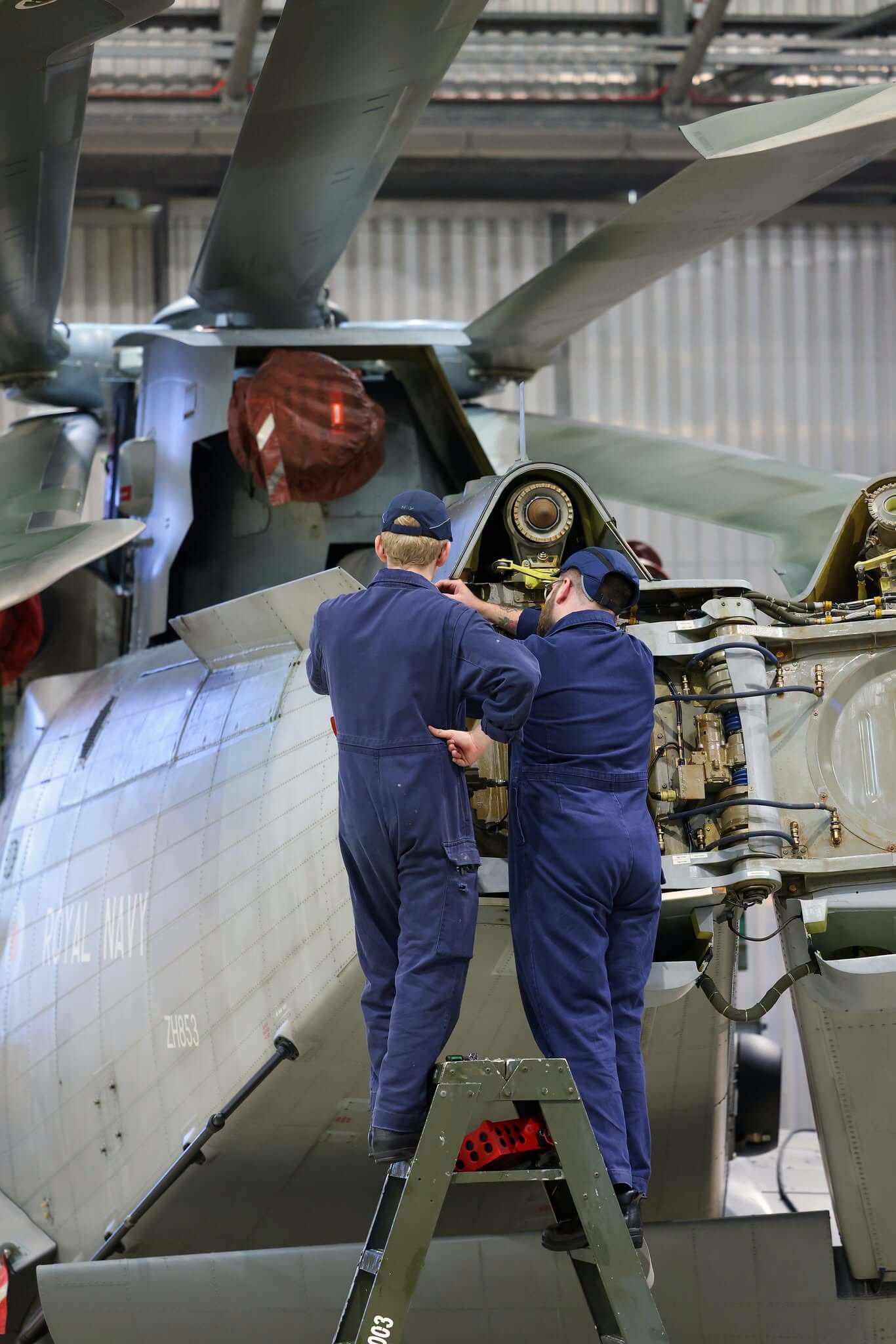 Two Royal Navy engineers working on a Merlin helicopter's rotor head