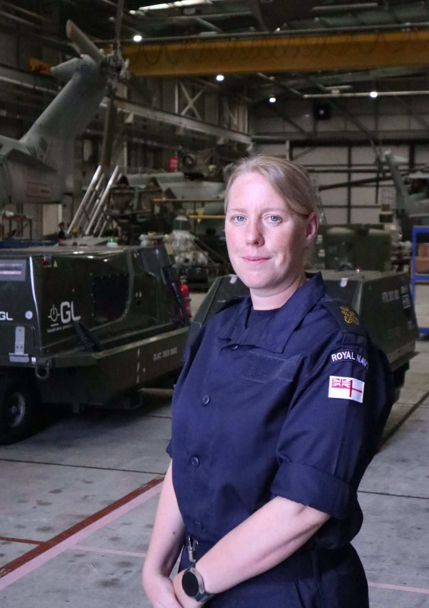 A Royal Navy petty officer air engineering technician stands in front of equipment in a Culdrose hangar