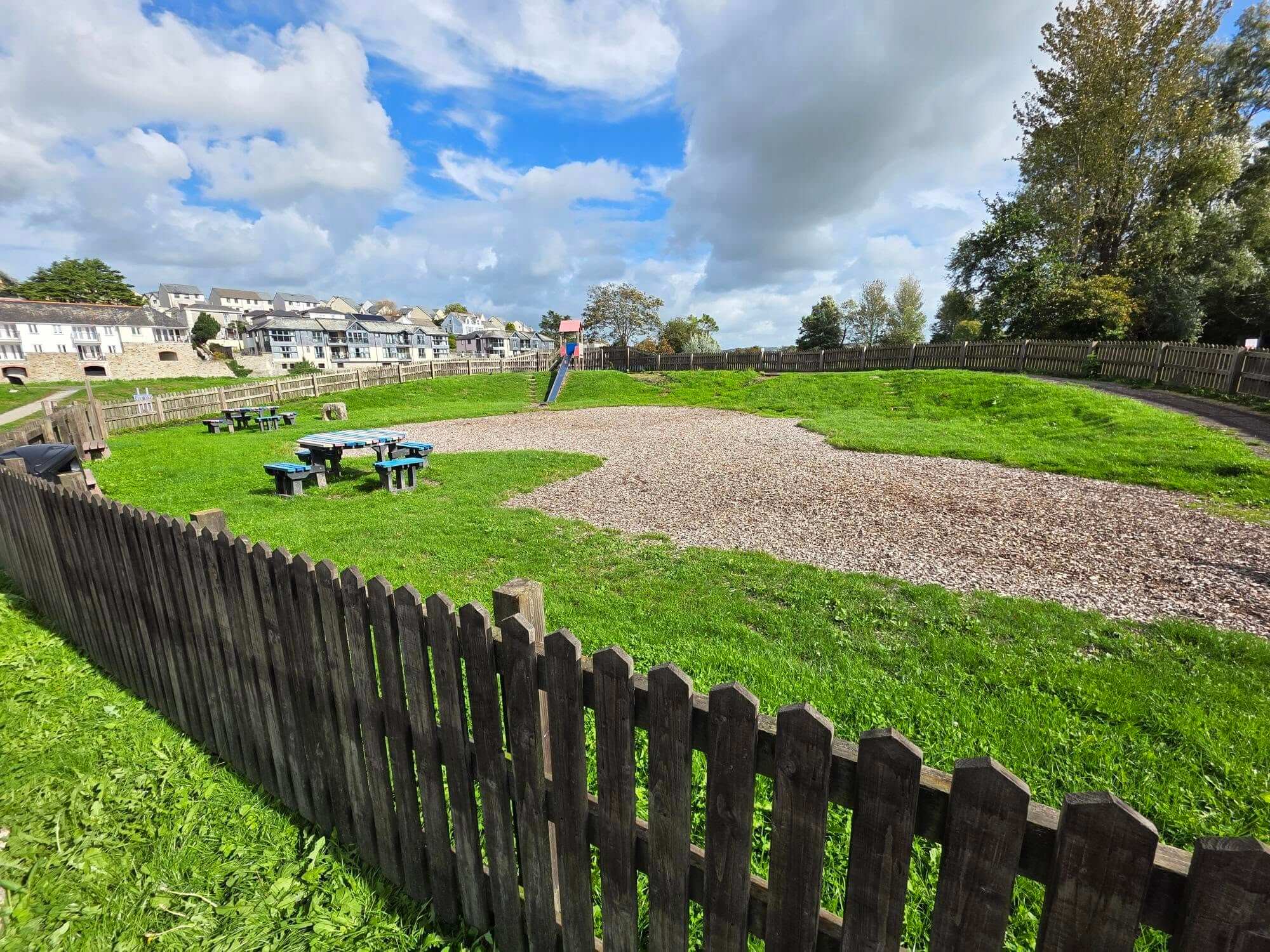 Jubilee Play Area in Wadebridge with bark chip, picnic tables and a slide behind a wooden fence