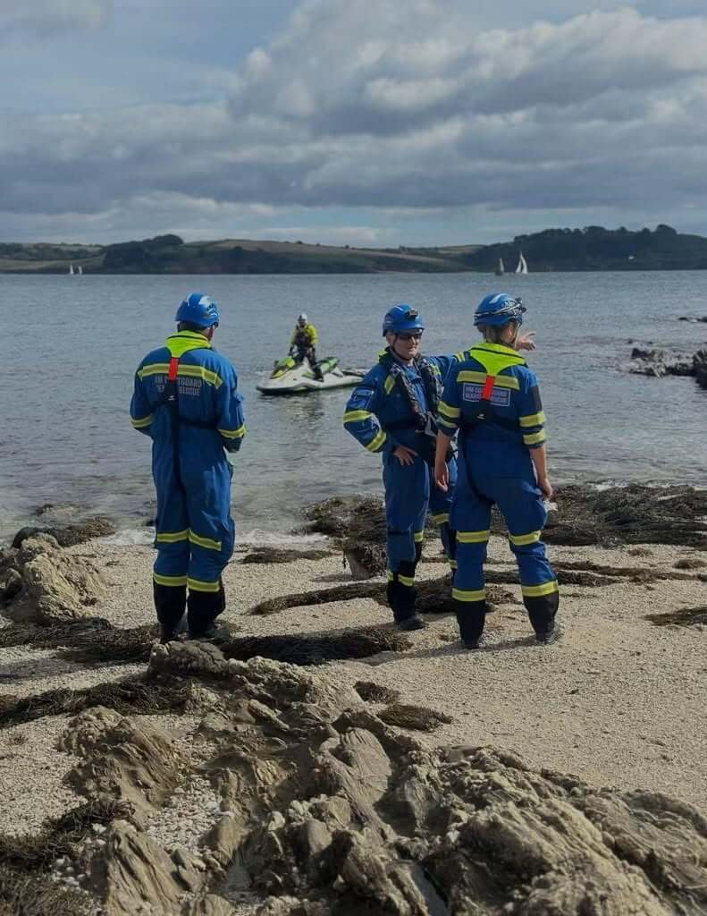 Falmouth Coastguard Rescue Team officers on a beach with a coastguard personal watercraft offshore