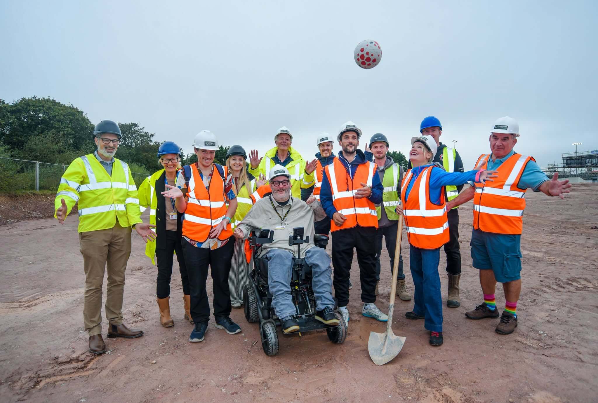 Group in hard hats and hi-vis throwing a football in the air at the Langarth pitch site