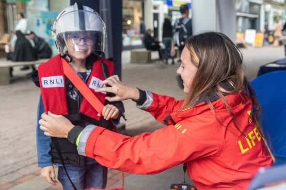 RNLI lifeboat crew member fitting a lifejacket and helmet on a young boy