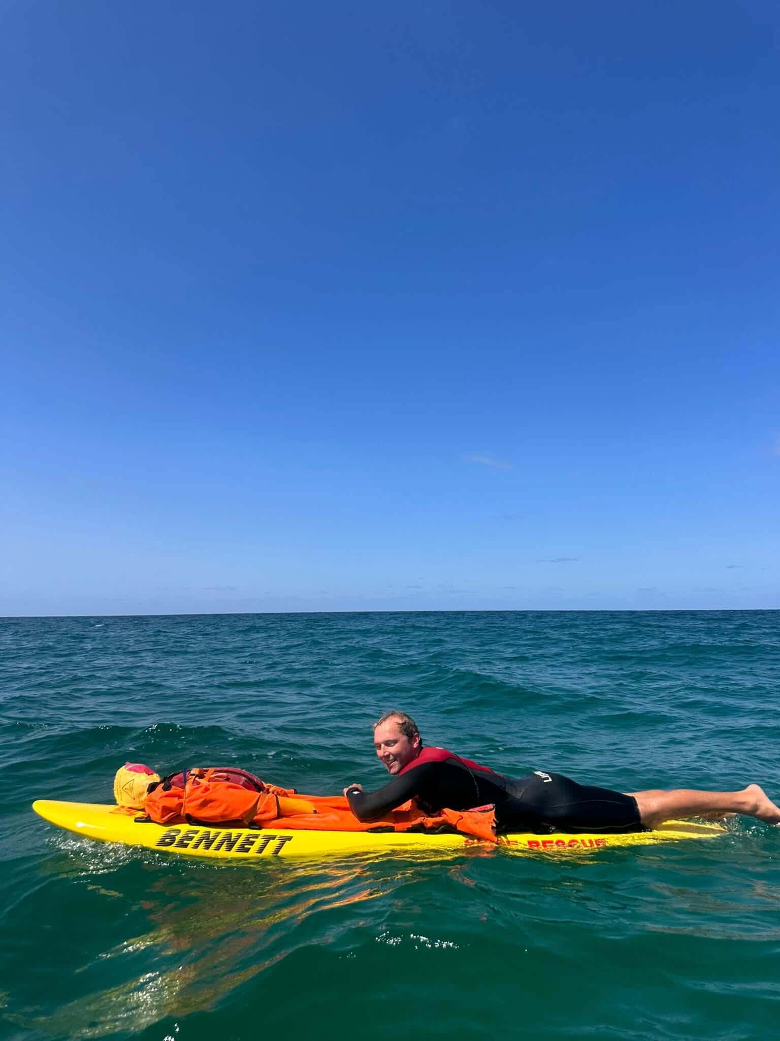 Lifeguard paddling a rescue board with a training casualty at sea