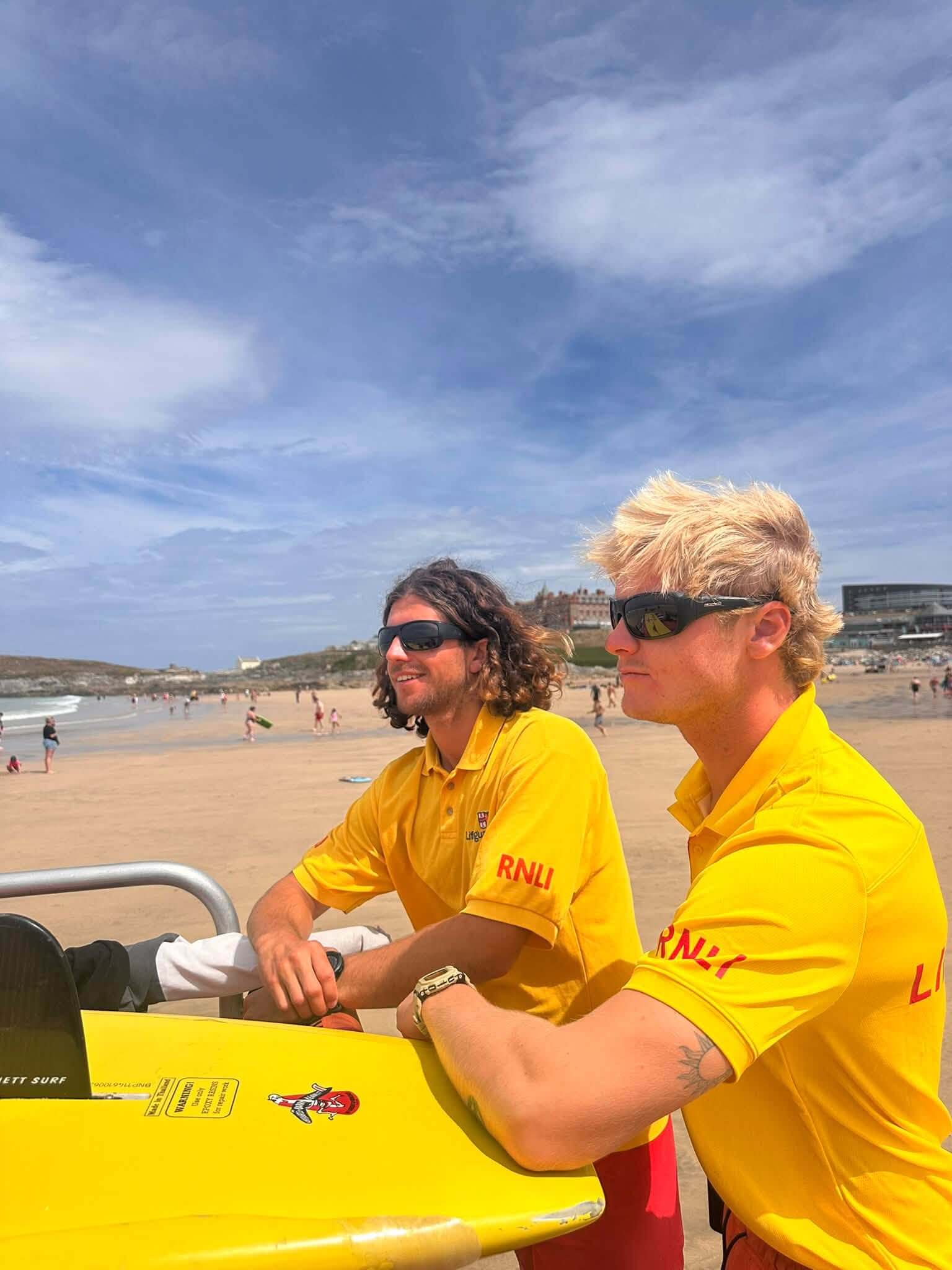 Two RNLI lifeguards in yellow tops watching a busy Newquay beach