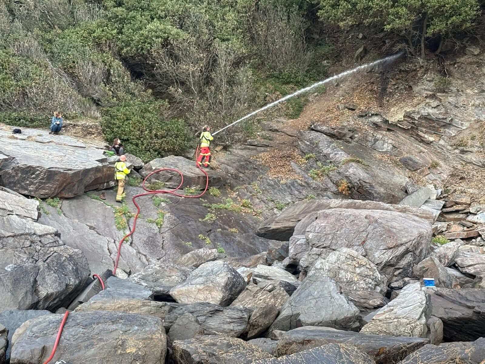 Firefighters with a hose line on the rocks between Grebe and Mawnan