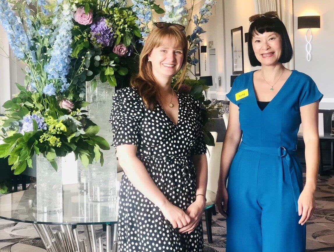 Pharmacist Yung Strawbridge standing with Abigail Wilson beside a large flower display