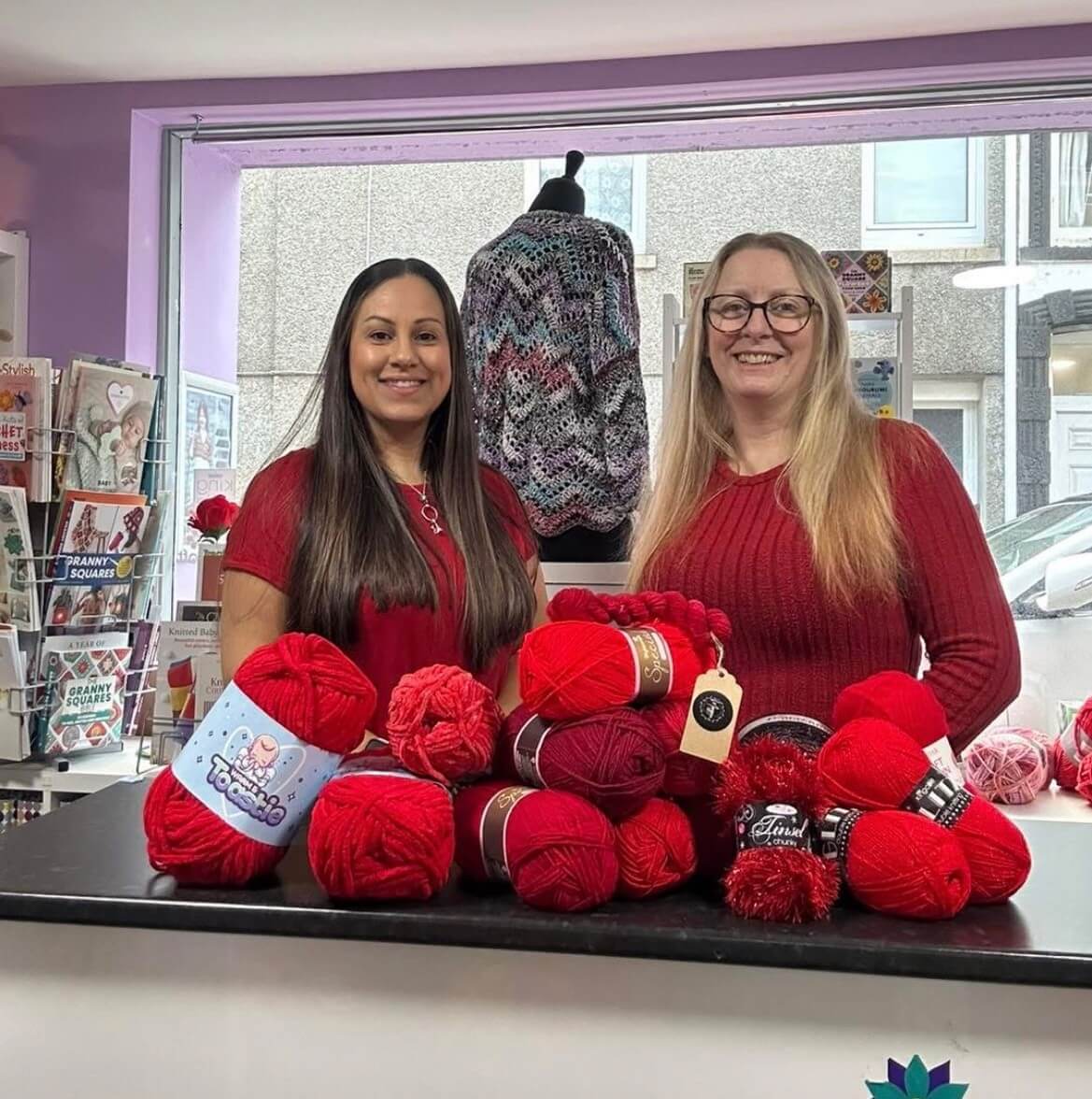 Two members of the A Darn Good Yarn team behind the counter with red yarn