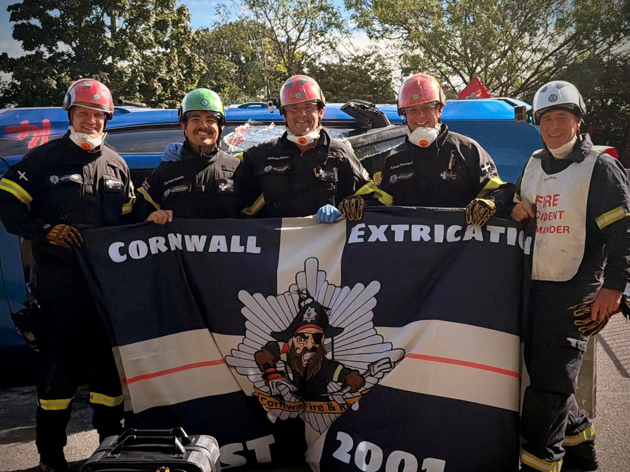 The Cornwall Fire and Rescue Extrication Team hold a Cornwall Extrication flag beside the rescue vehicles
