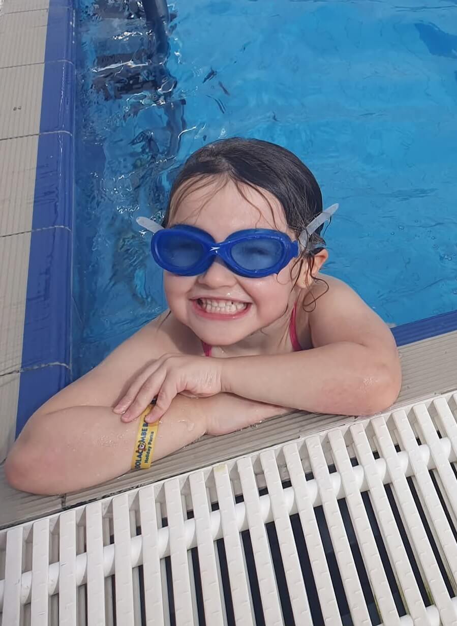 Grace smiling in swimming goggles at the pool edge
