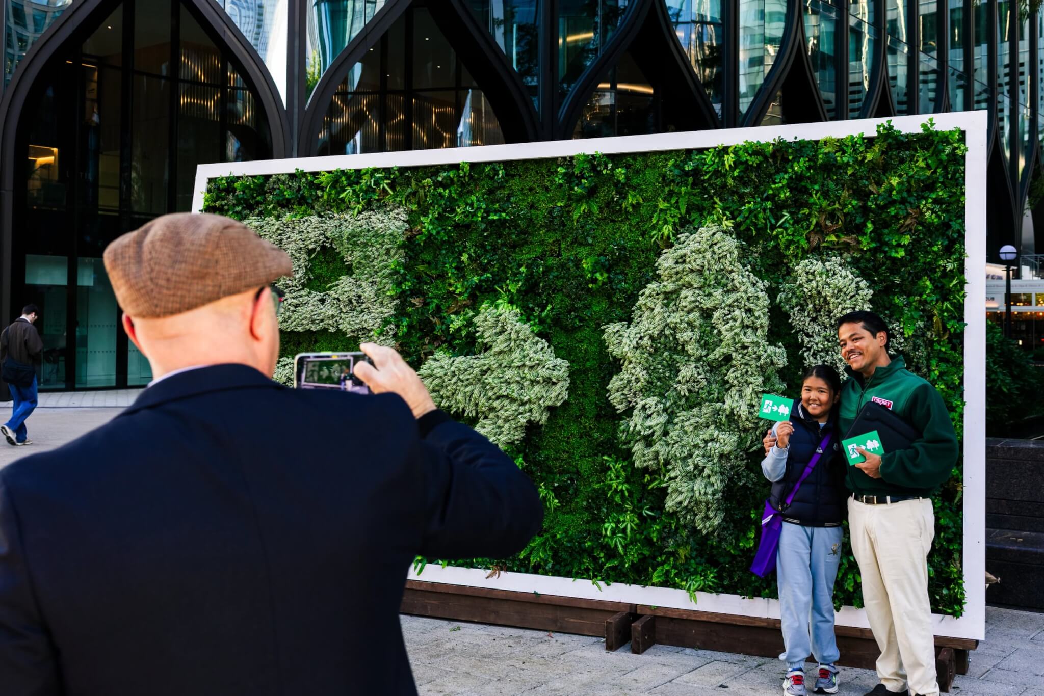 A member of the public photographs a couple posing beside the living sign
