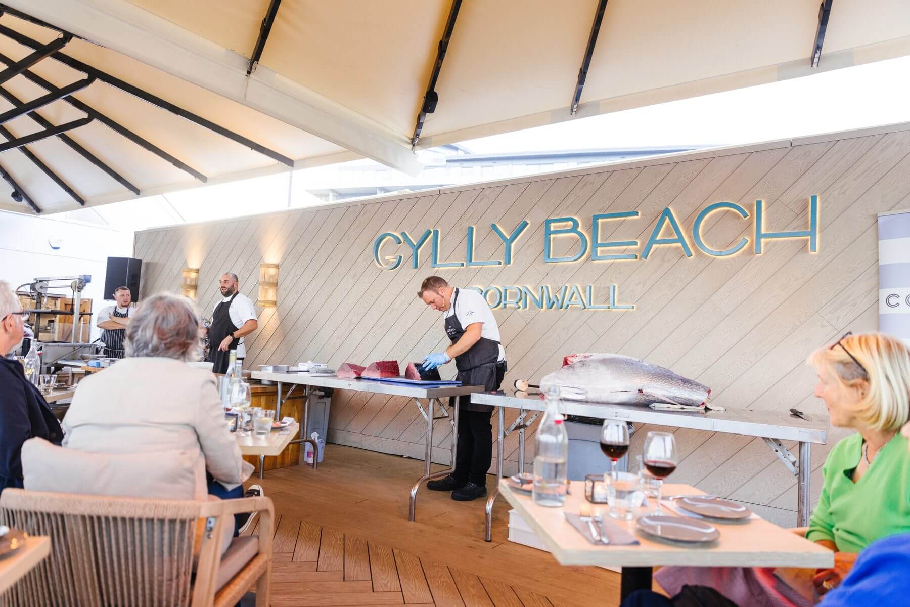 Diners watching a tuna being prepared under the awning at Gylly Beach