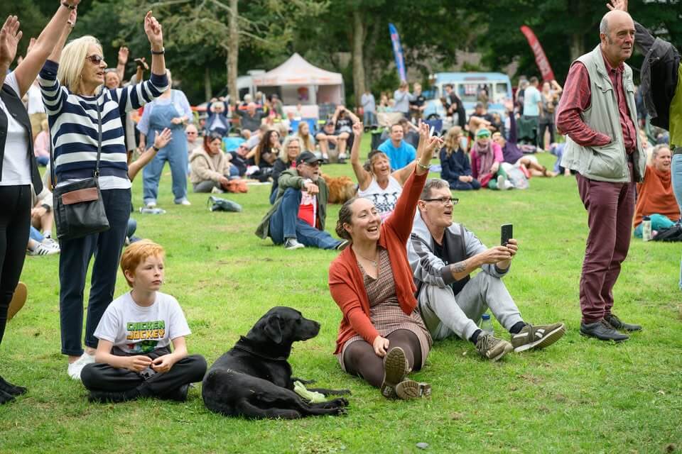 Festival-goers and a black Labrador on the grass at Camborne Green Fest