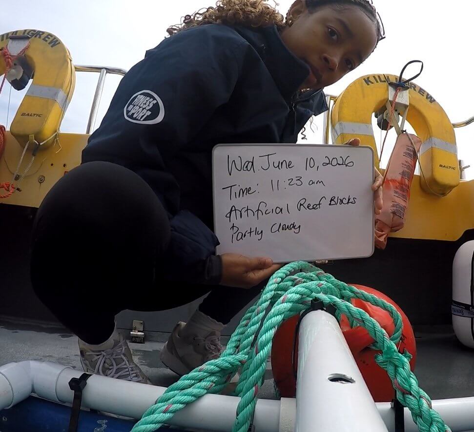 Khianna Lee on a boat holding a survey whiteboard beside the camera rig