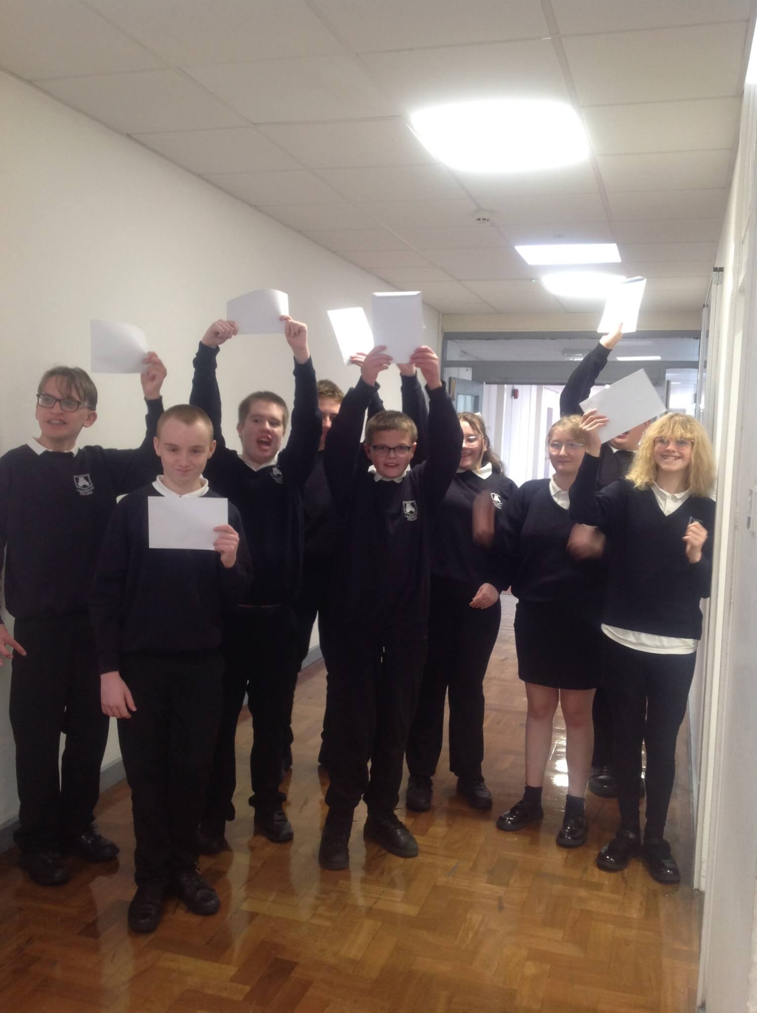 Launceston College ARB students in school uniform holding up their results in a corridor