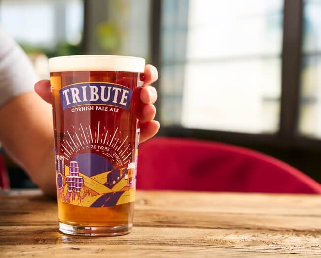 The new commemorative Tribute pint glass on a wooden pub table