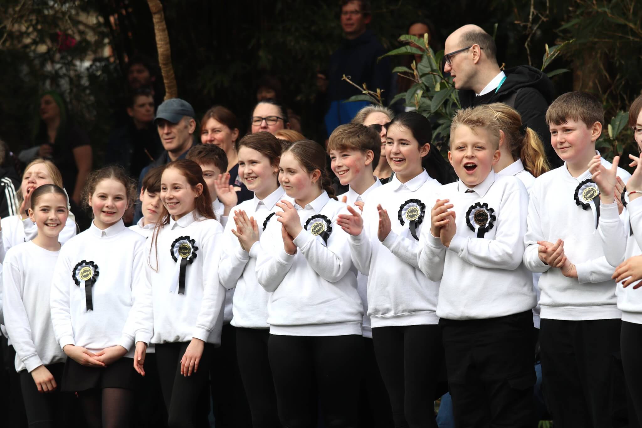 Schoolchildren in white jumpers and St Piran 2026 rosettes clap and cheer