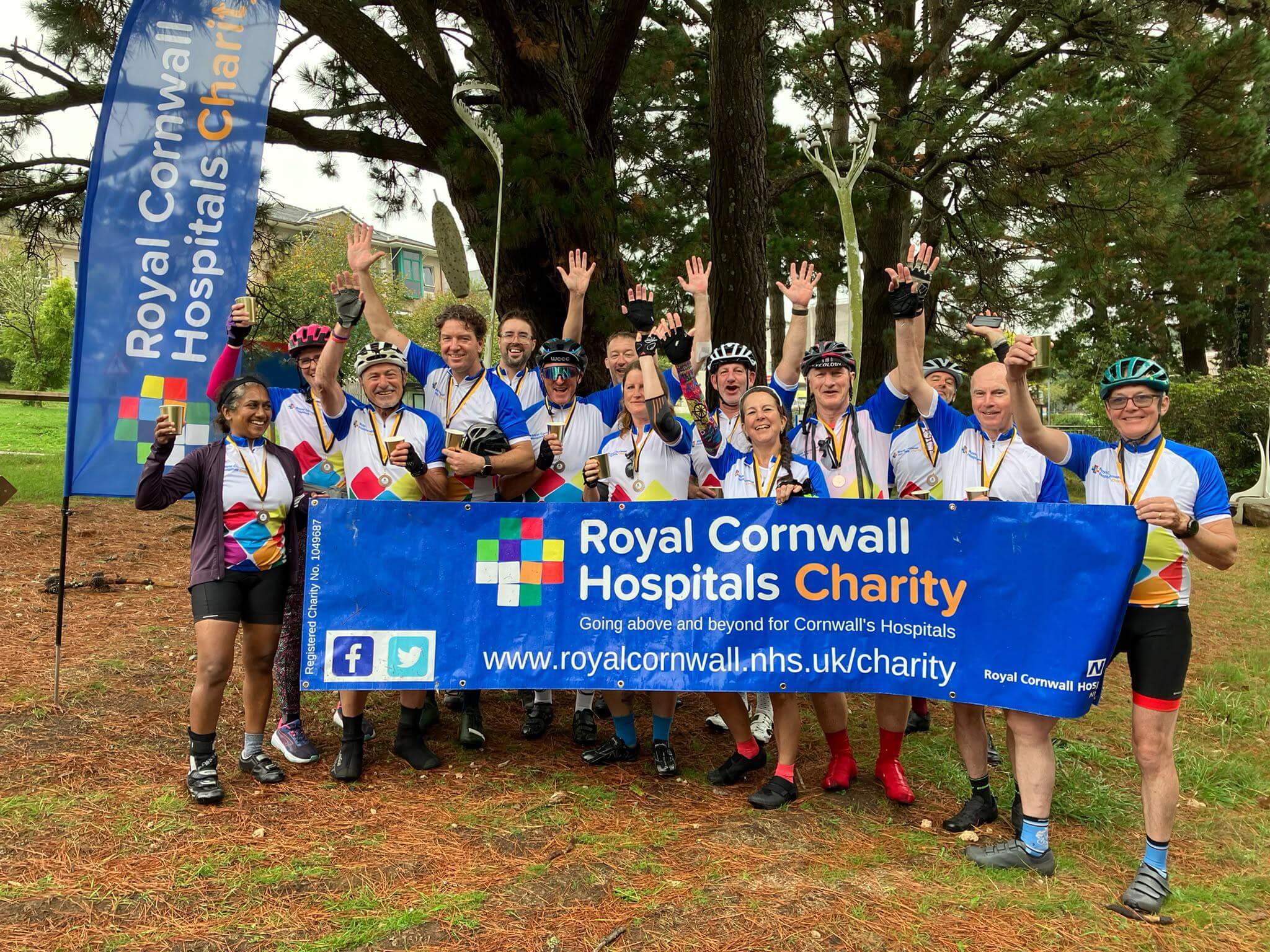 Pedal 4 Patients cyclists celebrating behind a Royal Cornwall Hospitals Charity banner